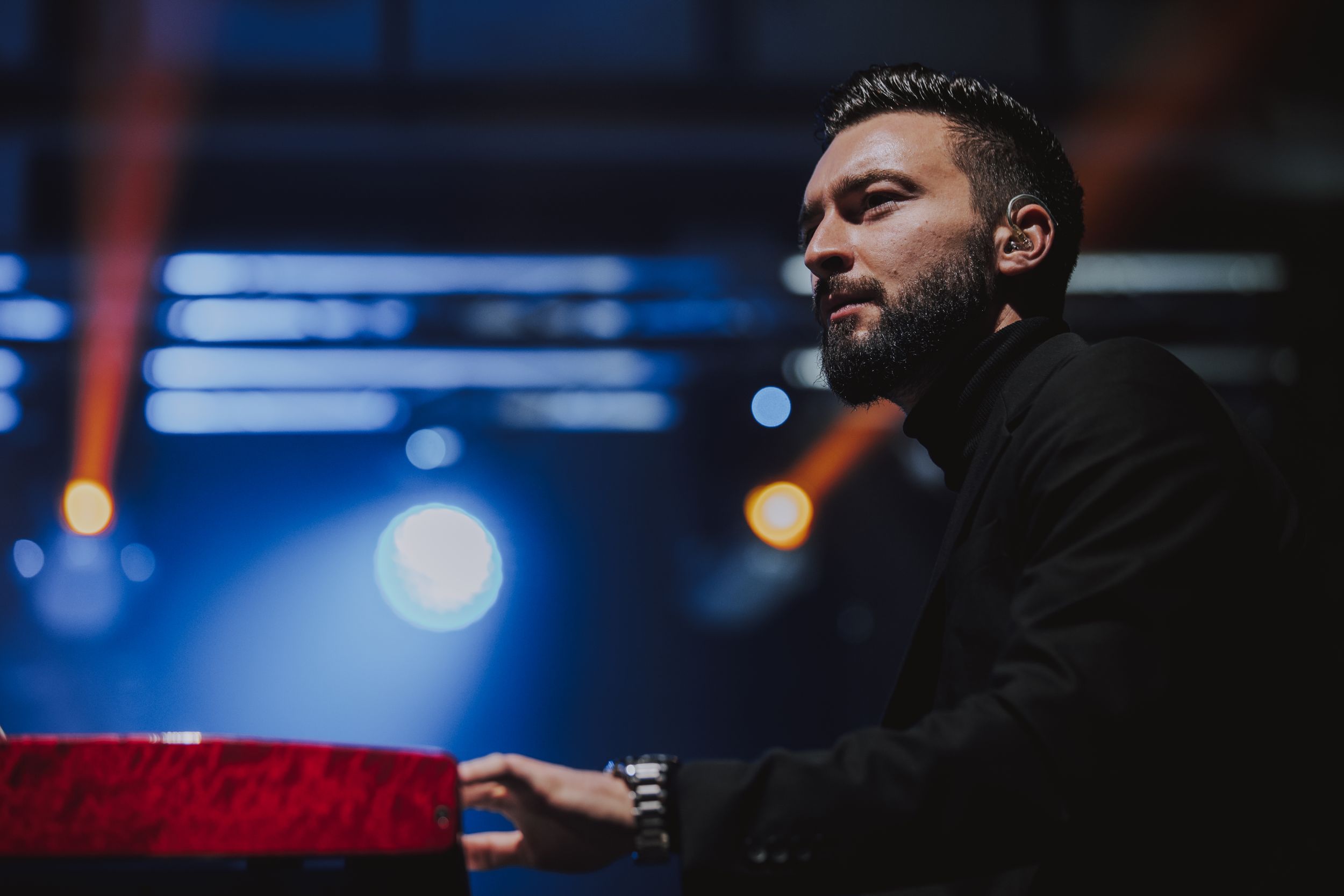 Performer playing keyboard on stage with blue lighting and modern stage design.