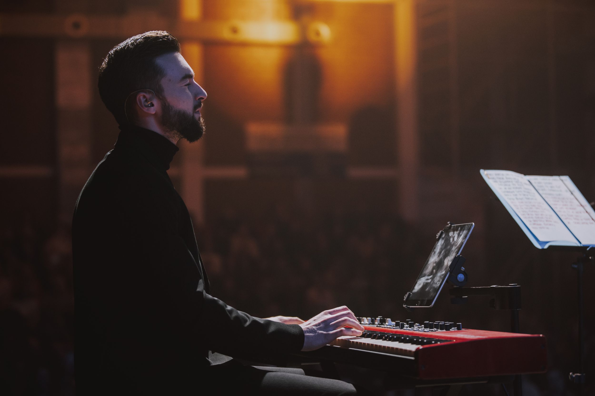 Musician plays keyboard at concert with sheet music and warm ambient lighting.