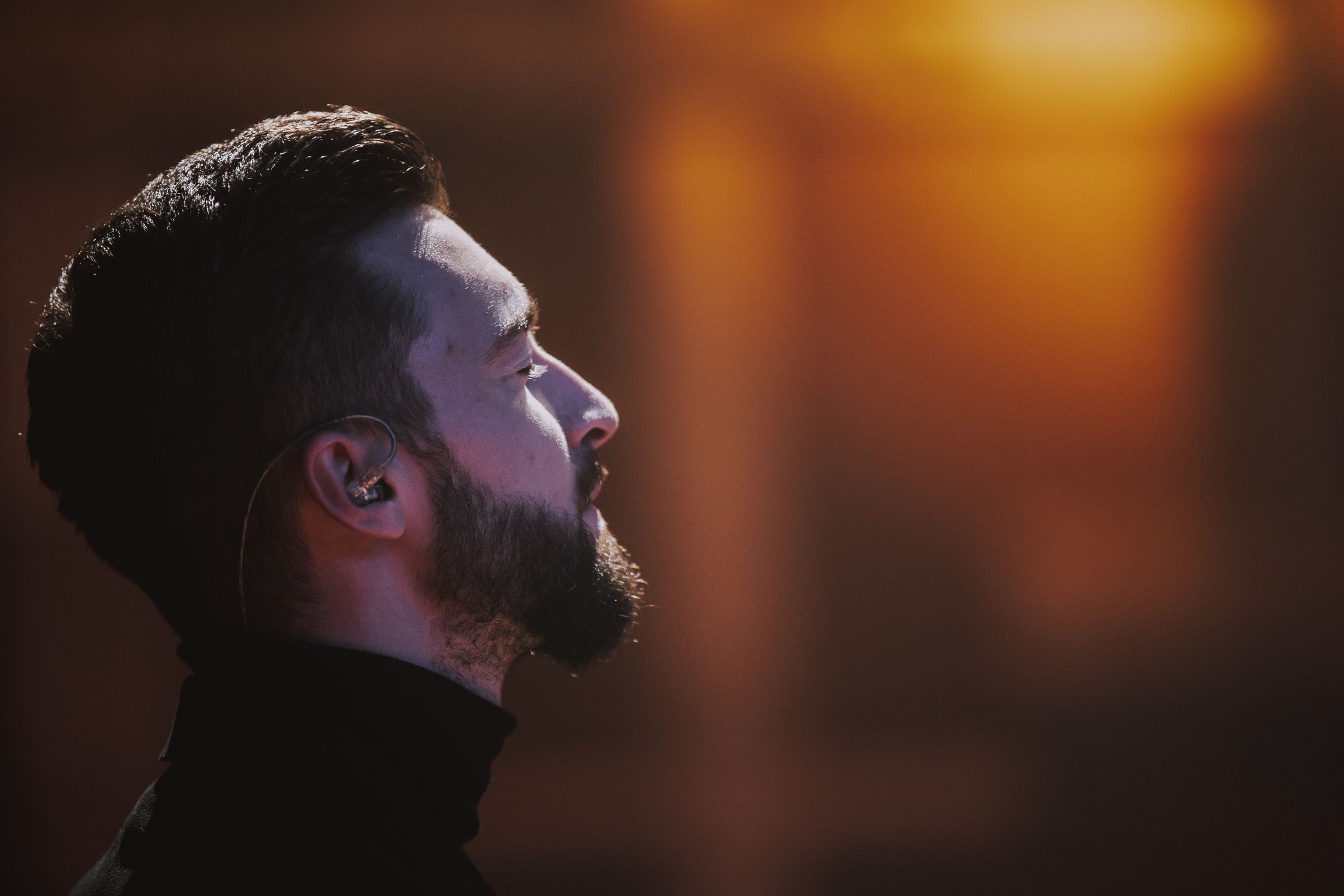 Side profile of performer in dark lighting with warm orange glow in background.