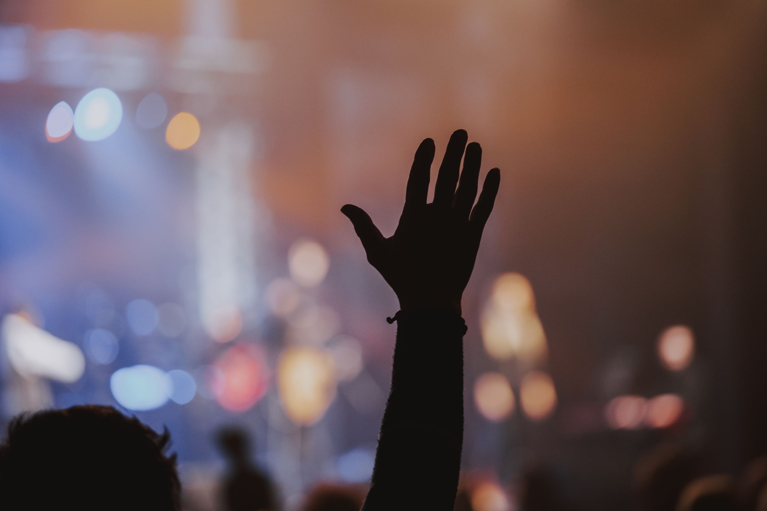 Silhouetted hand raised in worship during concert with bokeh lights in background.