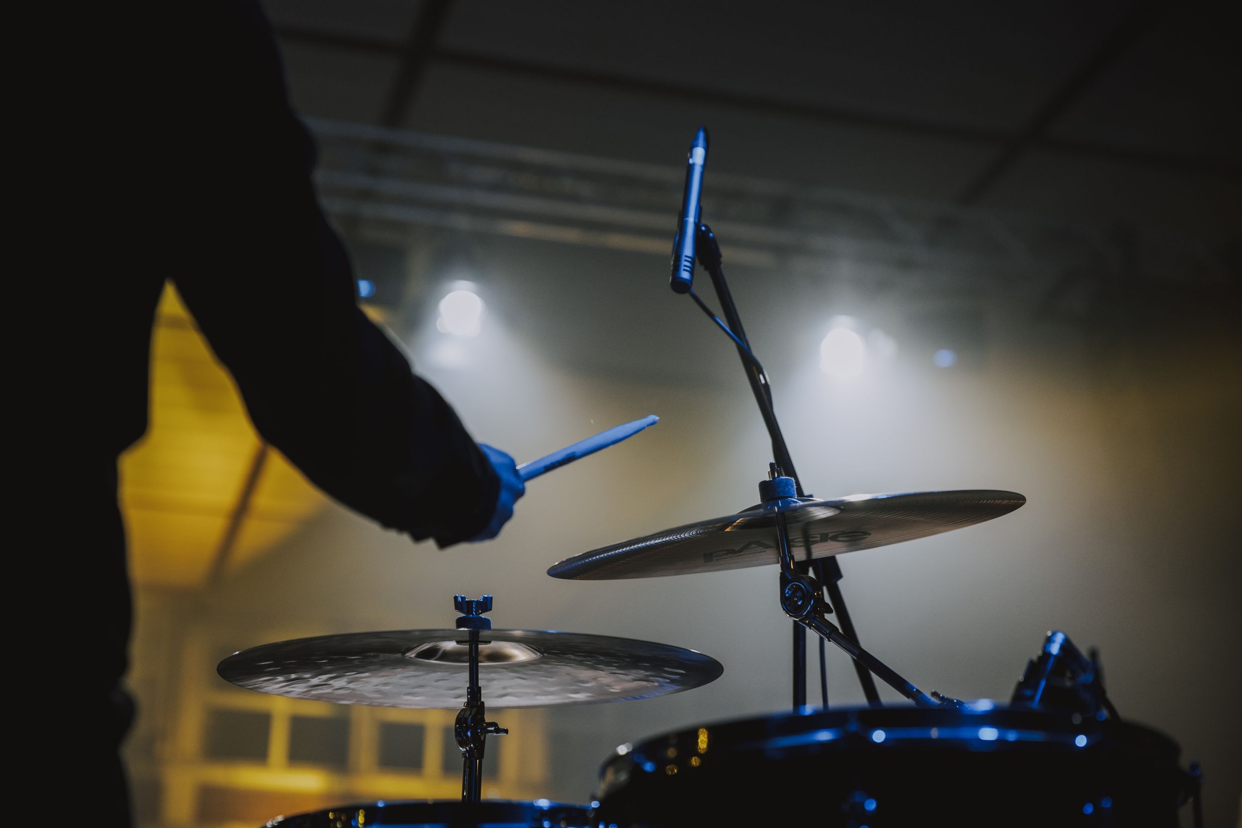 Silhouetted drummer playing cymbals with stage lighting effects.