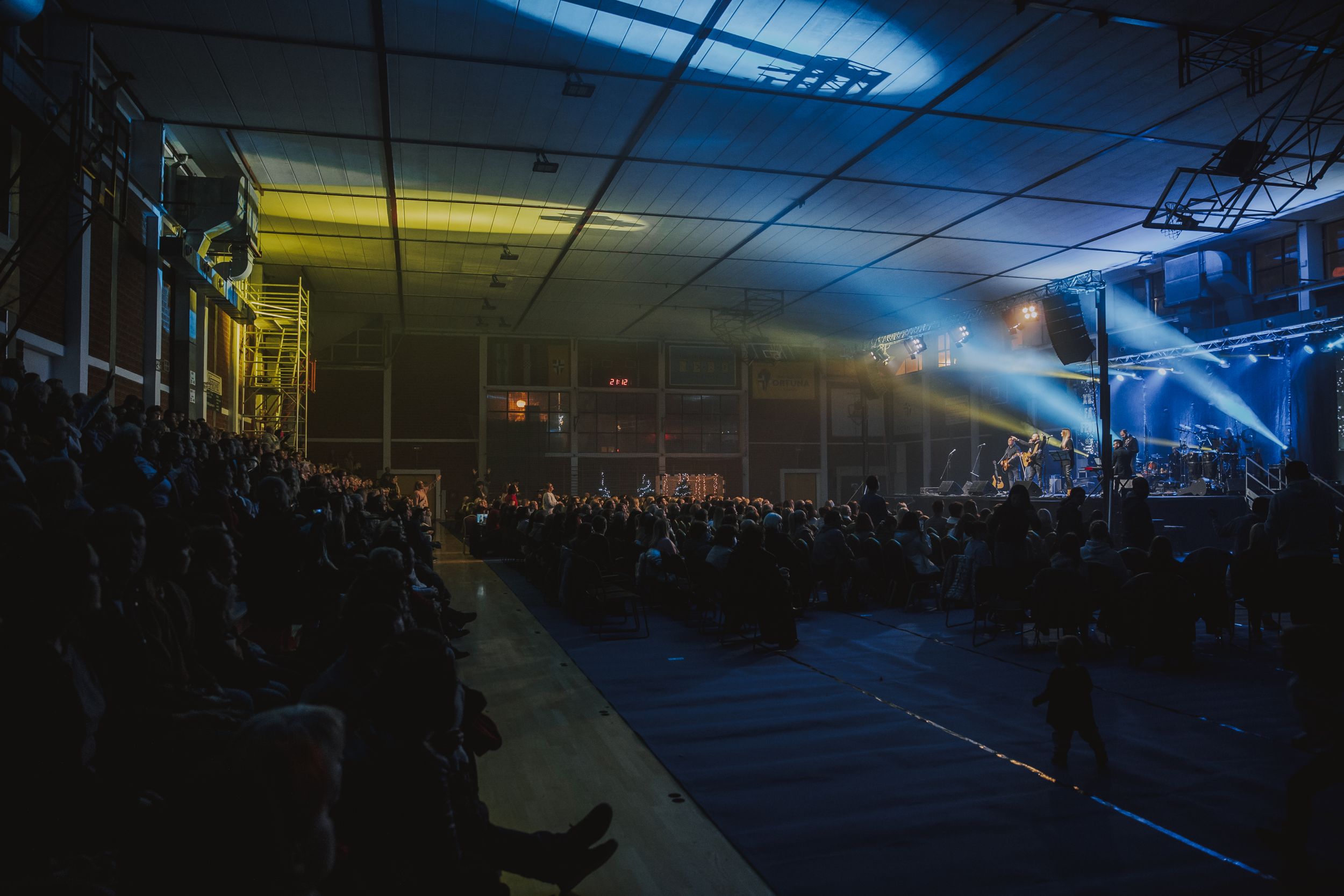 Wide shot of concert venue with crowd and dramatic blue lighting effects.