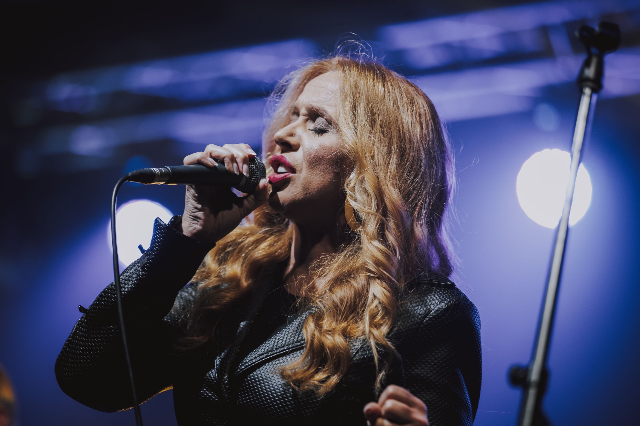 Singer performs on stage with microphone under dramatic blue concert lighting.