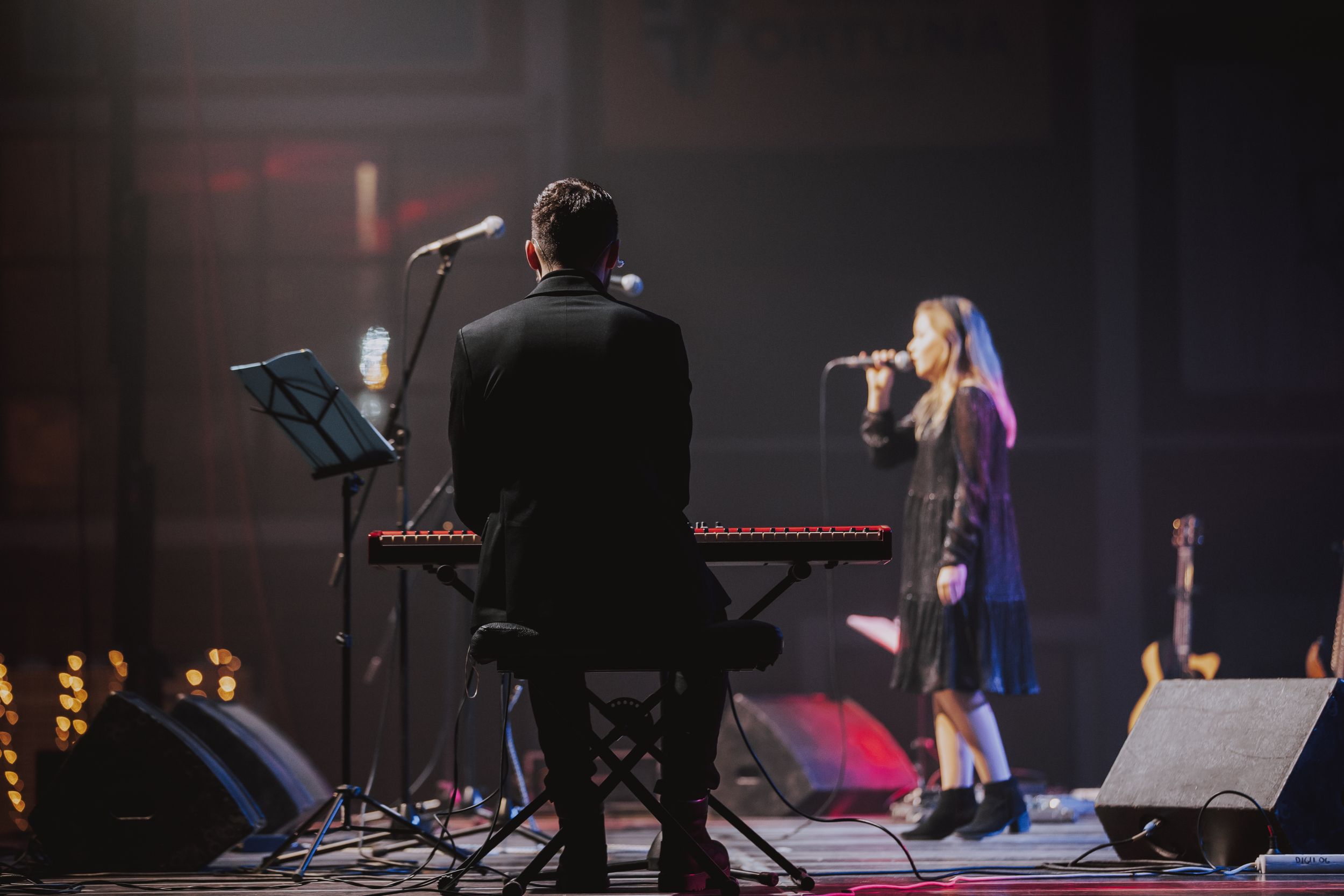 Musicians performing on stage with piano and microphone during indoor concert.