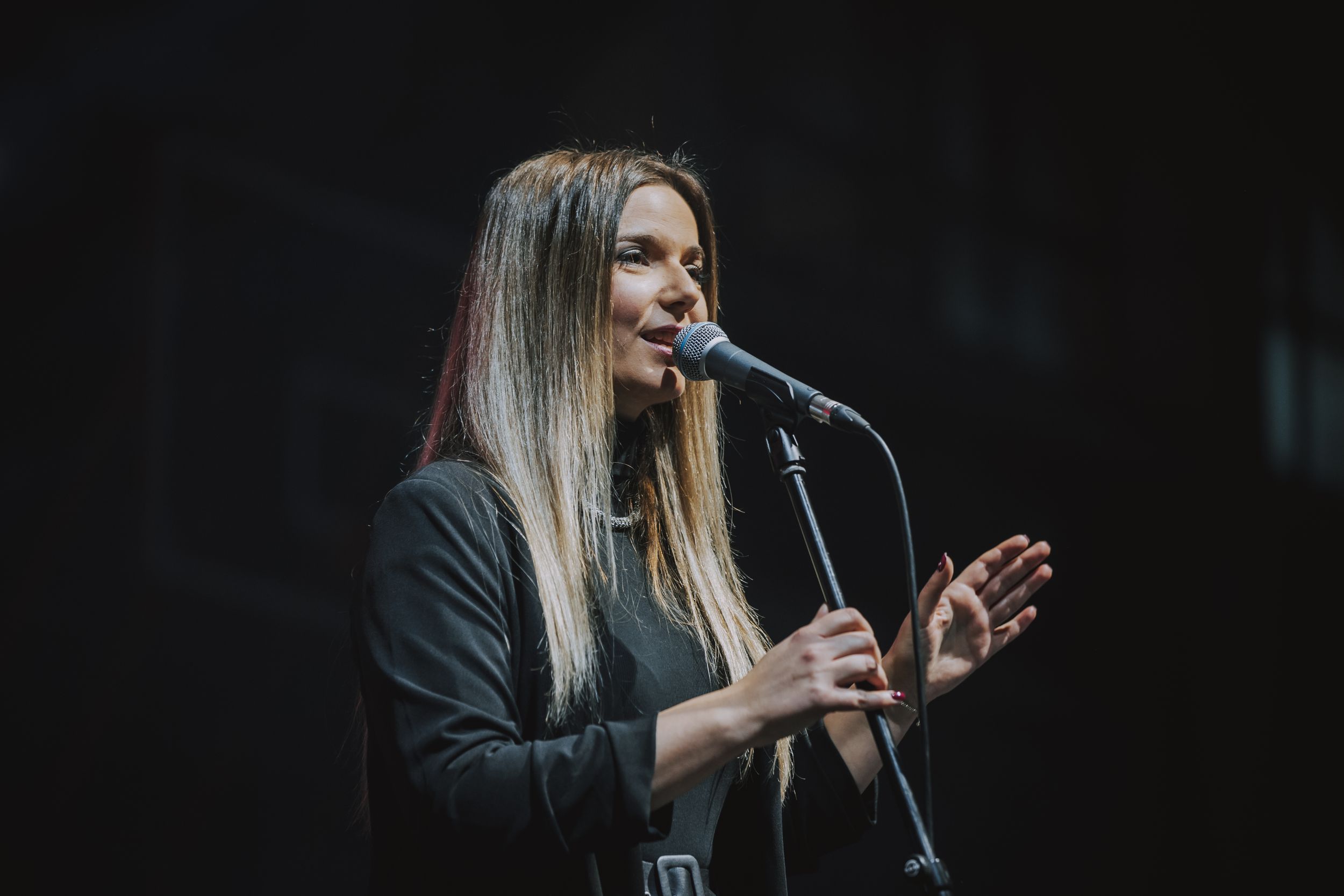 A vocalist performing on stage with an emotional hand gesture during a concert.