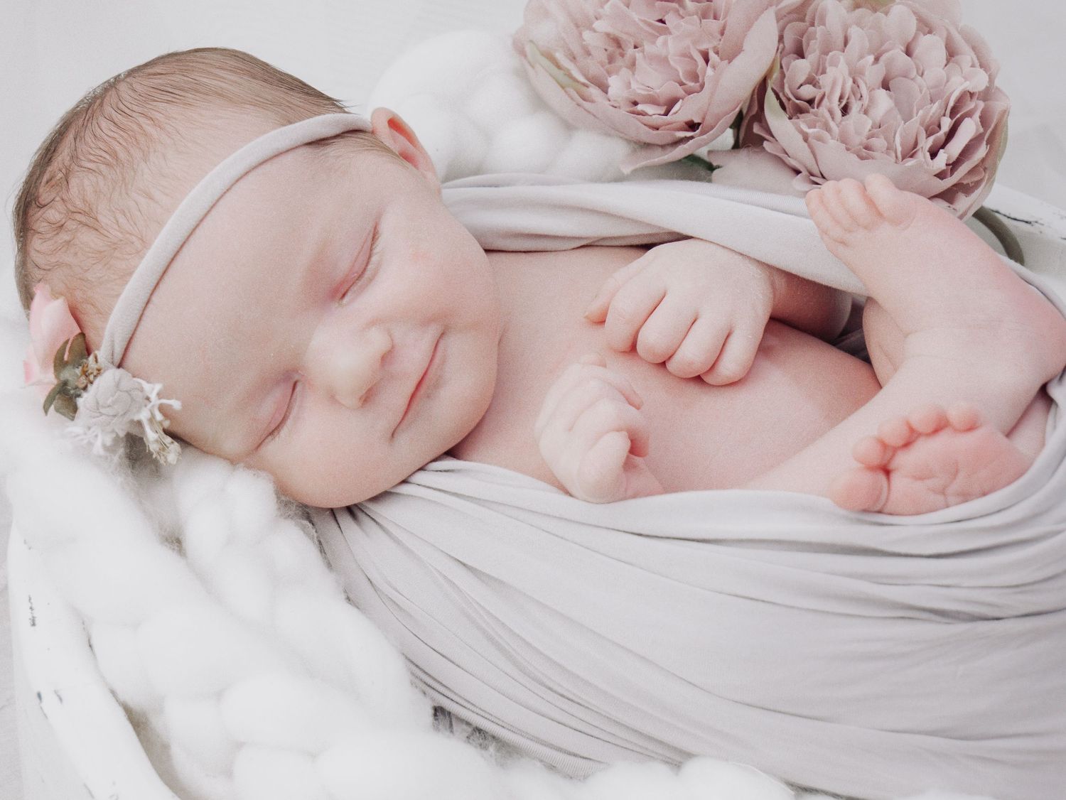 Sleeping newborn with headband wrapped in gray fabric with pink roses.