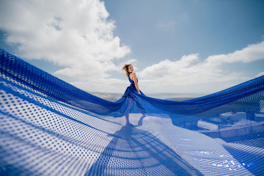 Dramatic blue fabric billows in the wind creating rippling patterns against a bright sky in Santorini.