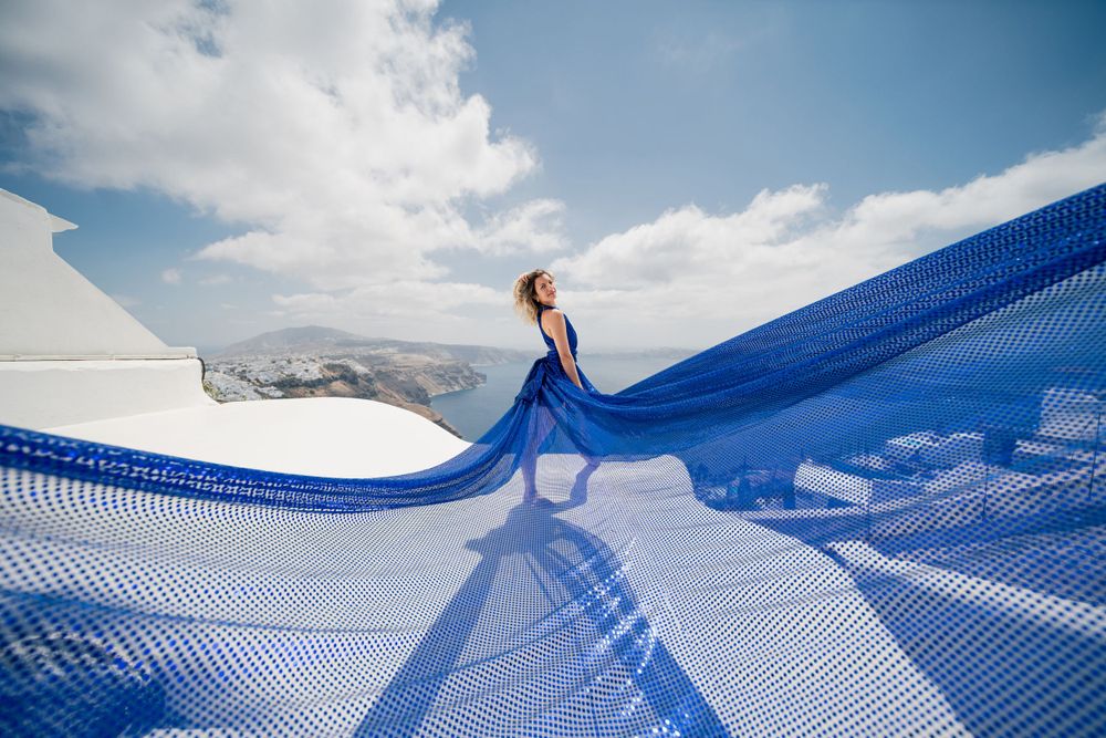 Royal blue fabric billows dramatically against white buildings and blue sky in Santorini.