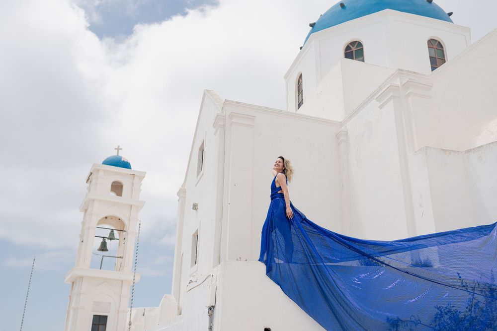 Blue fabric flows against traditional white Greek church architecture with bell tower.
