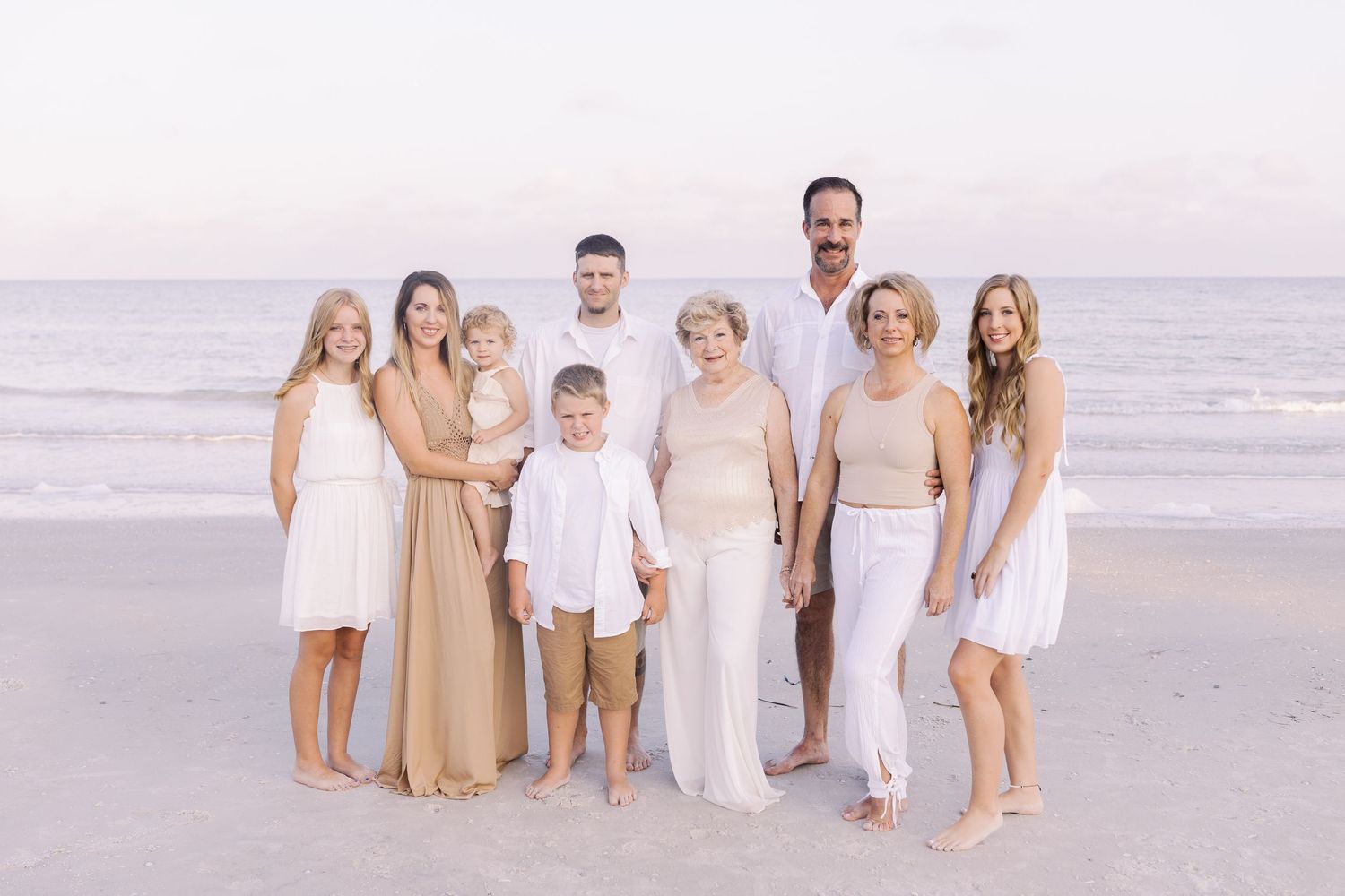 Group portrait on a beach with everyone wearing coordinated white and beige outfits.