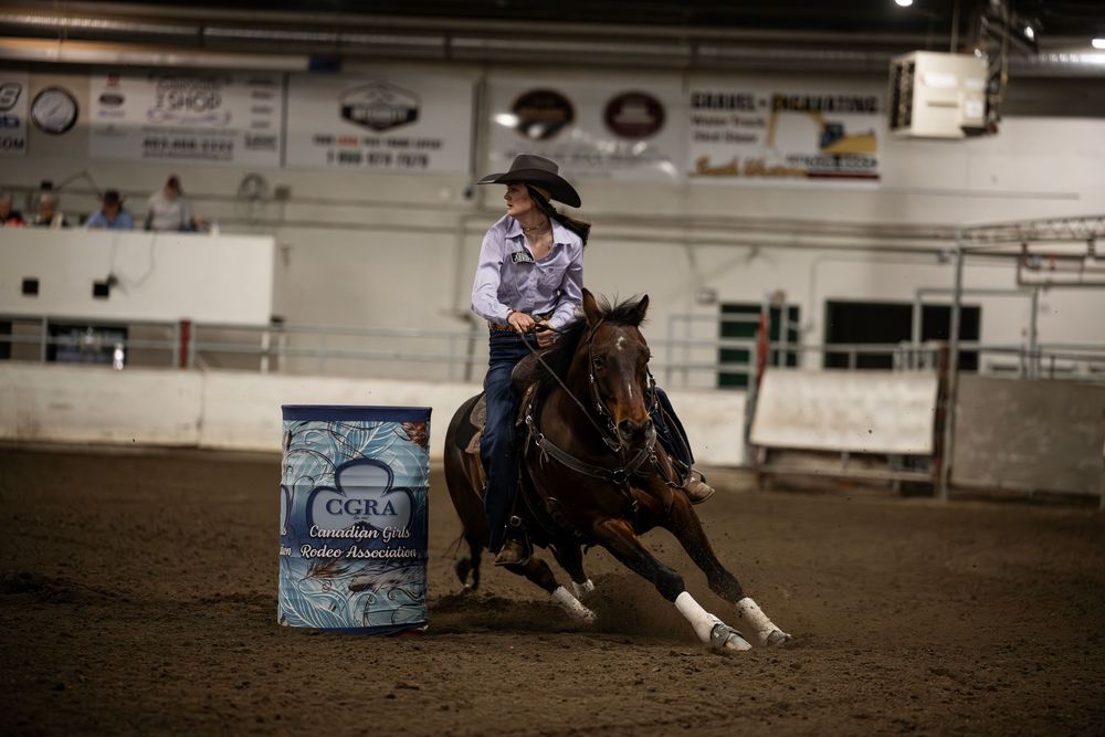 A barrel racer on horseback competes in a western rodeo arena during a competition event.
