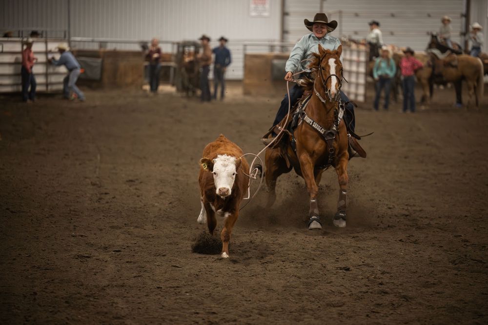 Rodeo competitors demonstrate skilled horsemanship during a western riding competition in an indoor arena.