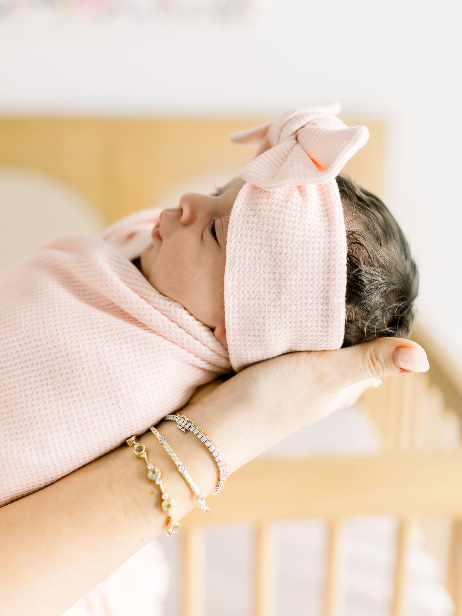 Sleeping baby wrapped in soft pink swaddle with delicate bow detail.