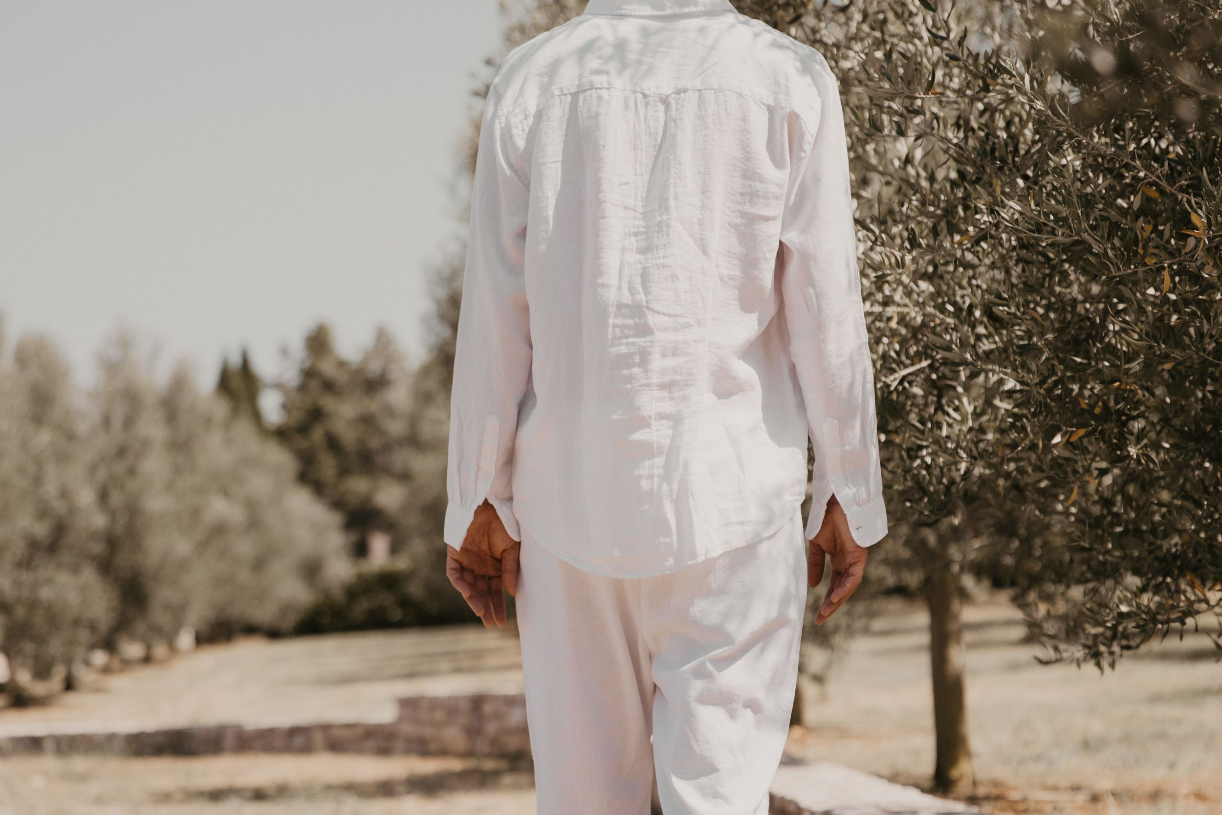 Back view of person wearing all white outfit walking in Mediterranean landscape.