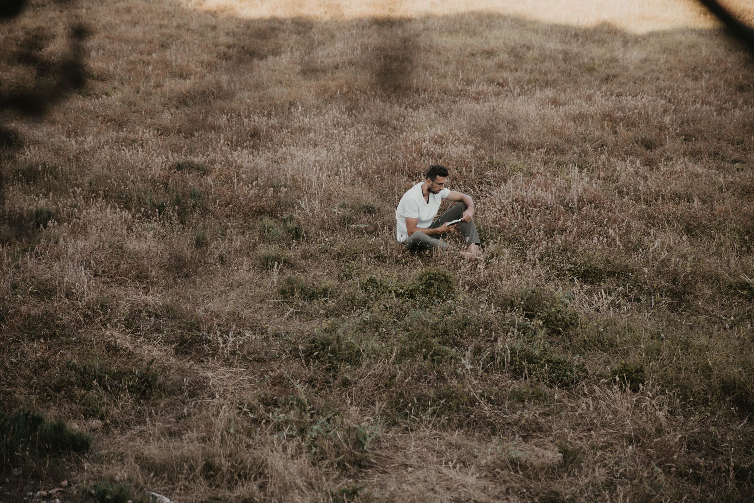 A solitary figure crouches thoughtfully on a grassy hillside at dusk.