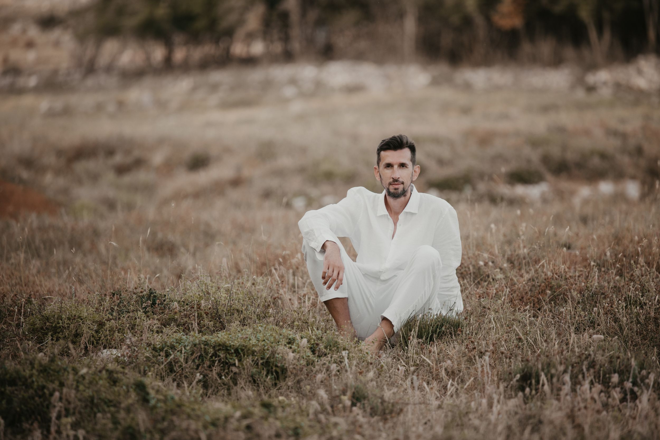 A person in white clothing sits in a field during golden hour.