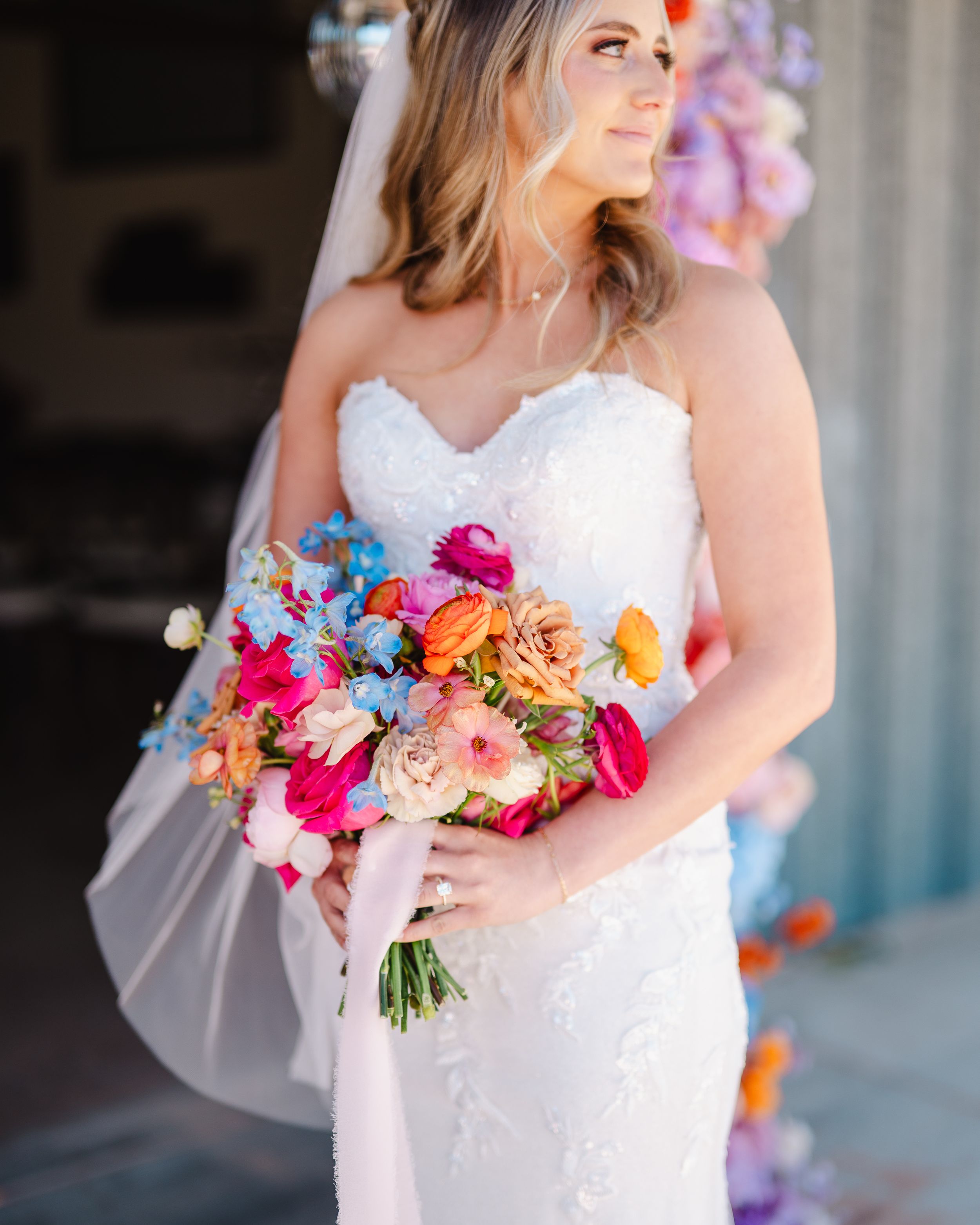 Bride in white strapless gown holding vibrant bouquet with pink and orange flowers.