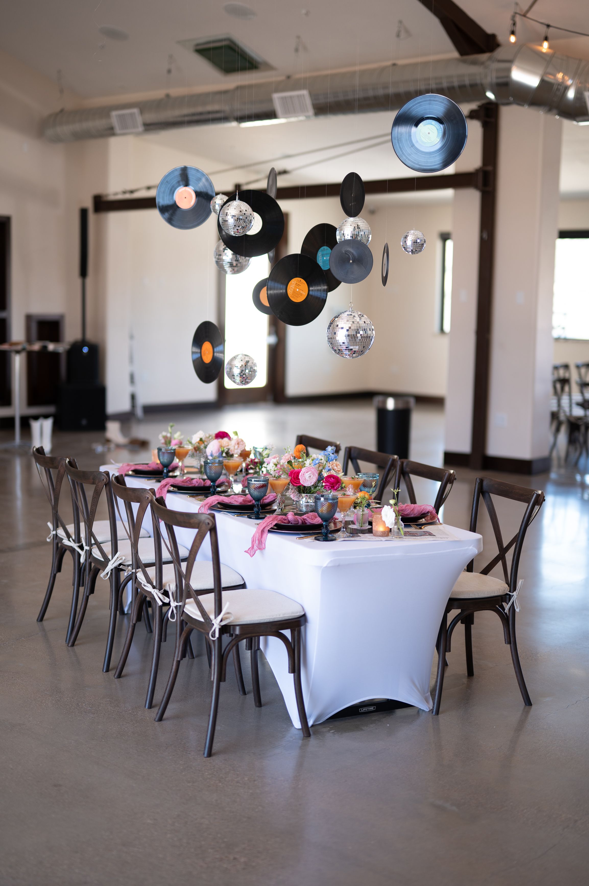 Modern reception table setup with hanging vinyl records and disco balls as decor.