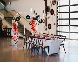 Wedding reception setup with vinyl records hanging from arch and white tablecloths.
