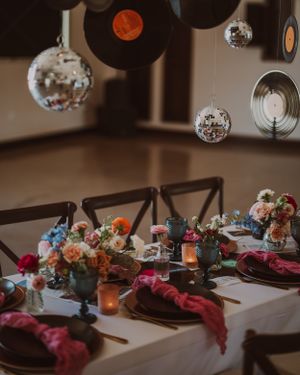 Elegant wedding reception table with disco balls, vinyl records, and colorful floral arrangements.