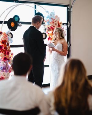Wedding ceremony with vinyl record decorations and colorful floral arch.