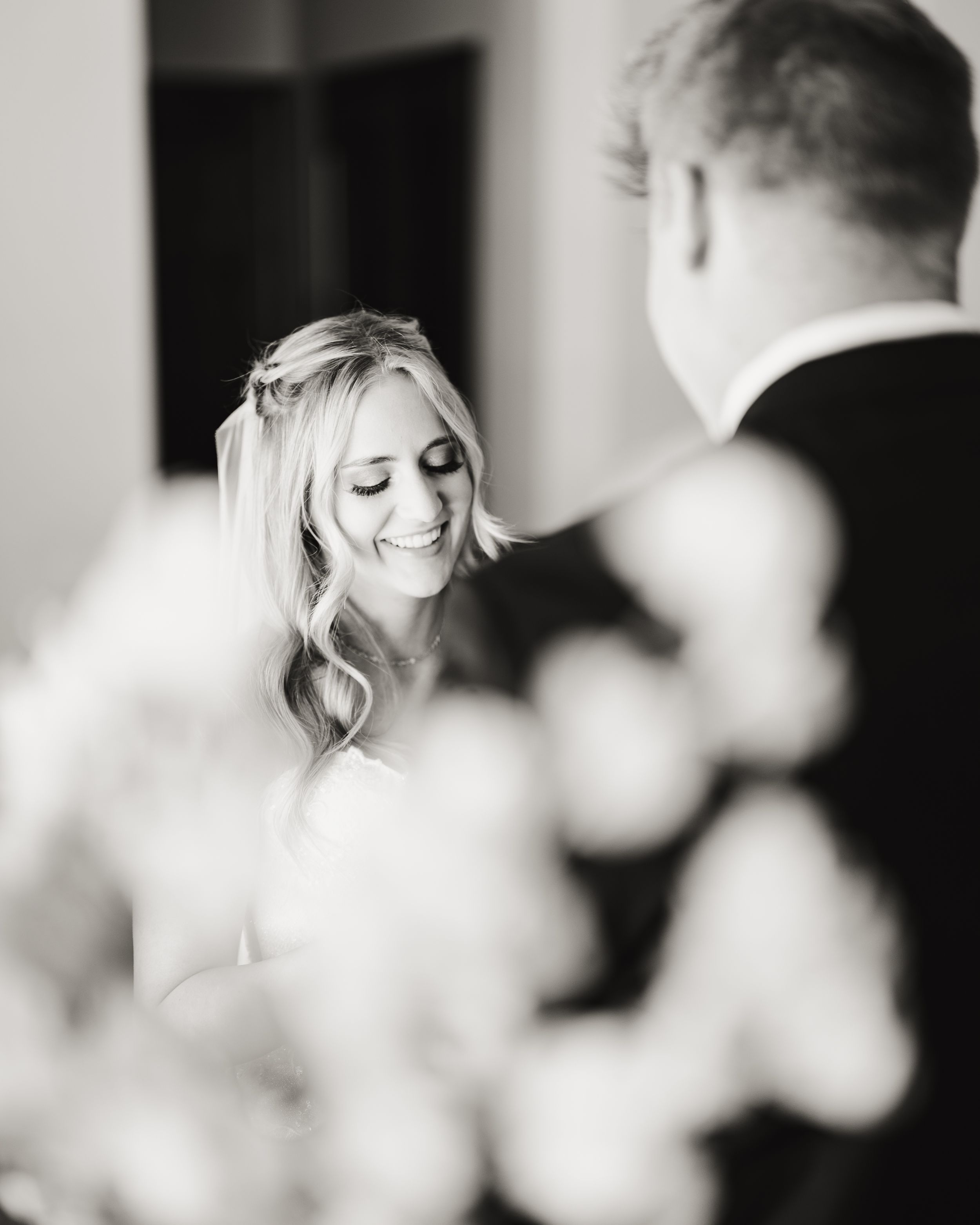 Black and white wedding portrait showing bride's joyful expression with elegant styling and soft lighting.