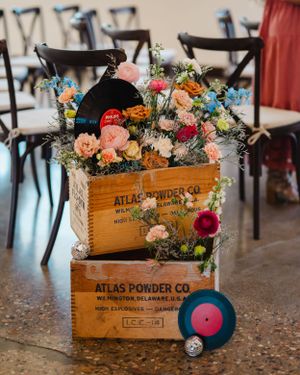 Vintage wooden crates filled with colorful flowers and vinyl records create unique wedding decor arrangement.