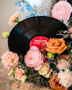 Vintage vinyl record surrounded by pink and peach roses in romantic wedding centerpiece arrangement.