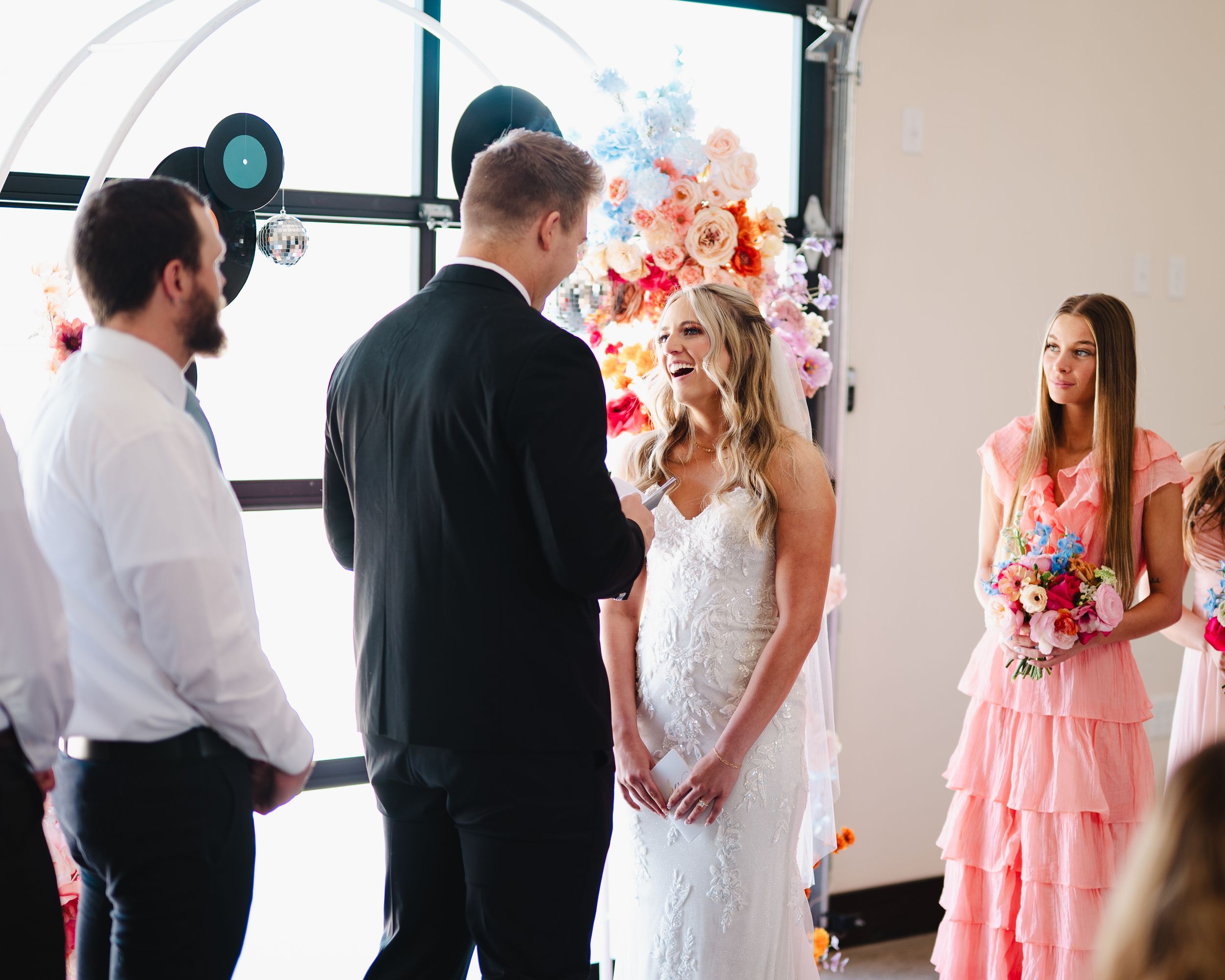 Wedding ceremony in bright venue with vinyl record decorations and colorful floral arrangements.