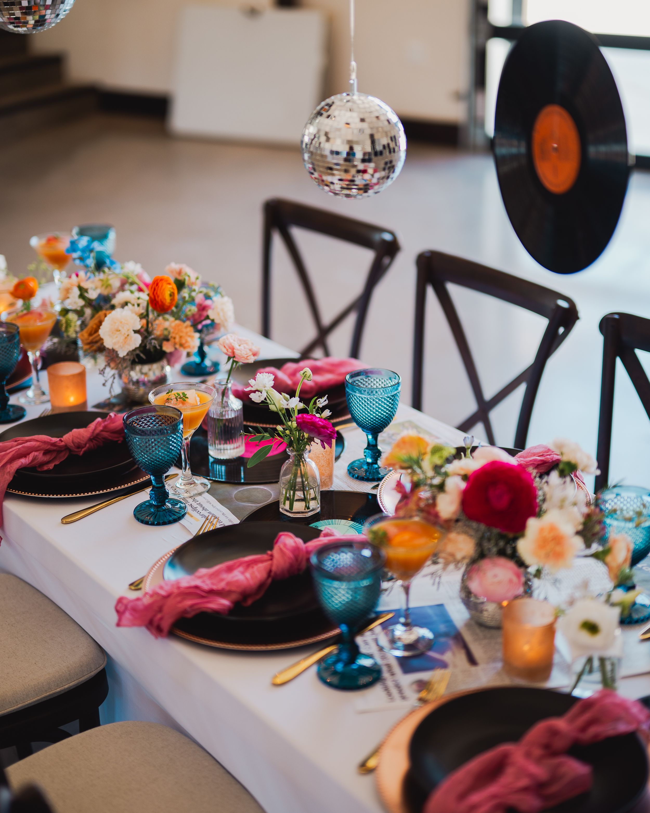 Wedding reception table decorated with vinyl records, disco ball, and bright blue glassware.