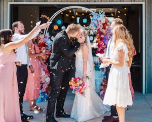 Wedding guests toss confetti as newlyweds kiss under modern arch with record decorations.