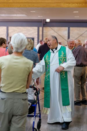 A minister in traditional vestments engages with parishioners in a church hallway.