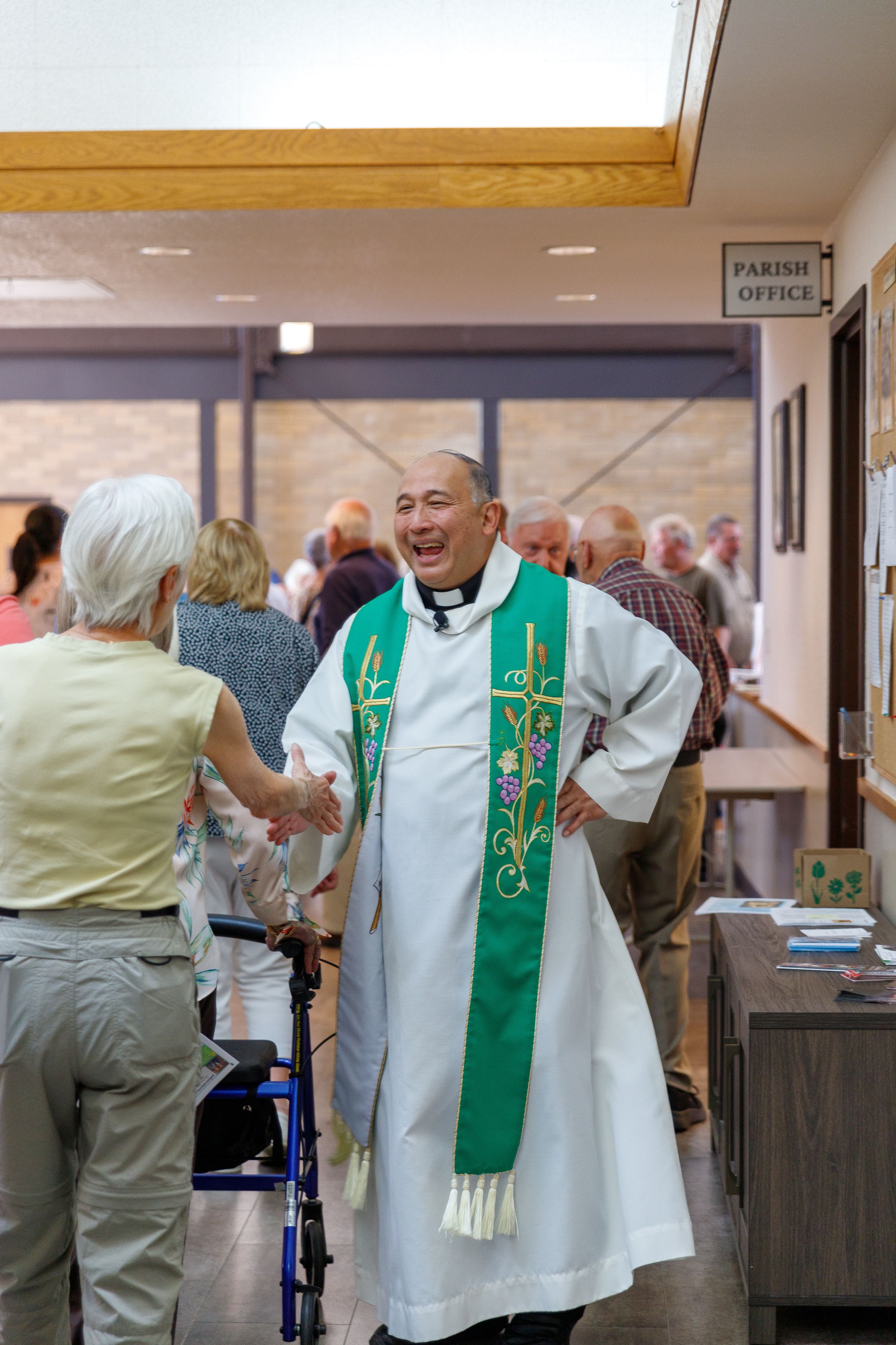 A clergy member in ceremonial robes stands near the parish office during a church gathering.