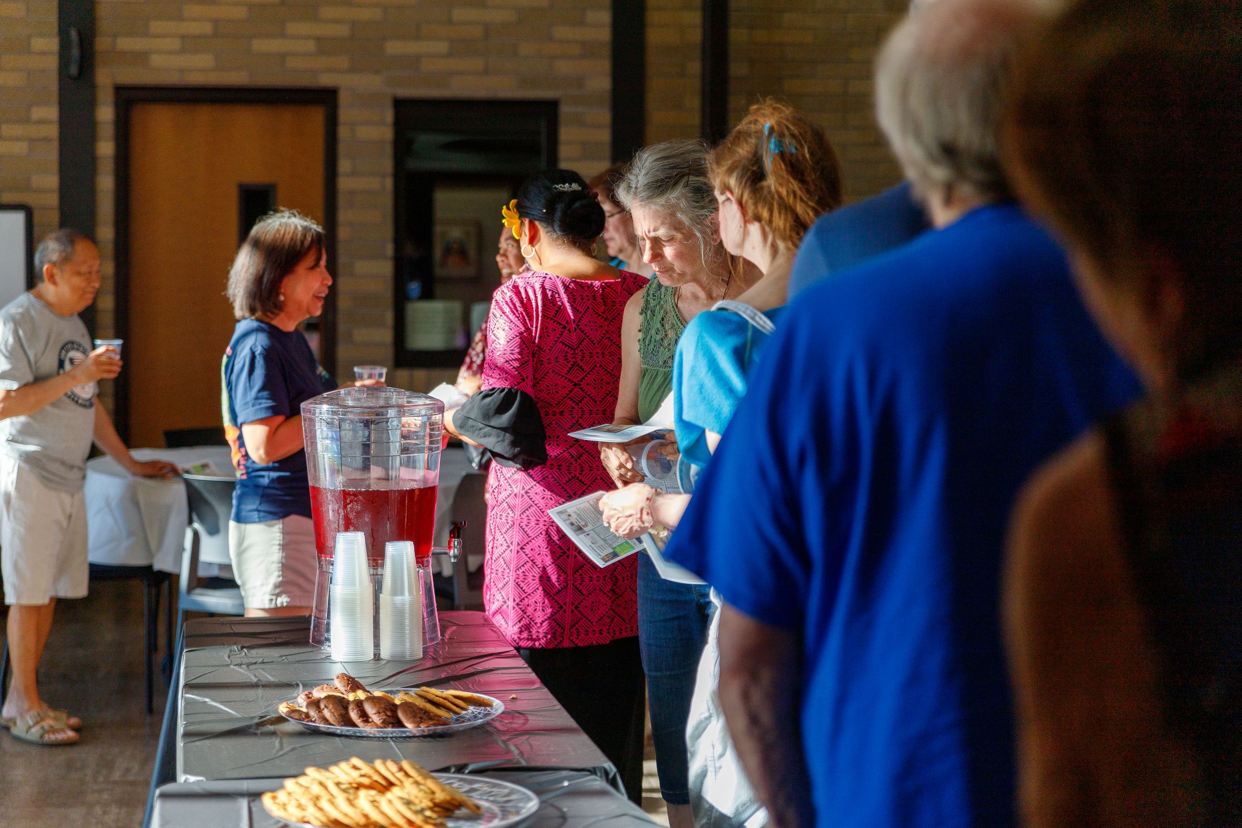 People line up at a buffet table with pies and refreshments during a church social event.