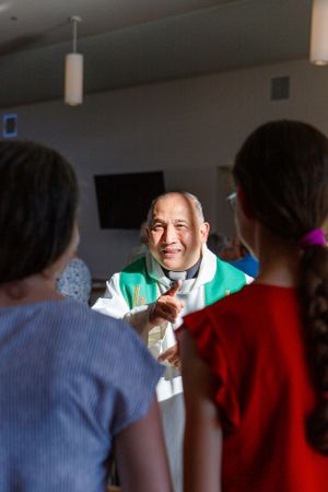 A spiritual leader in green vestments smiles while engaging with visitors.