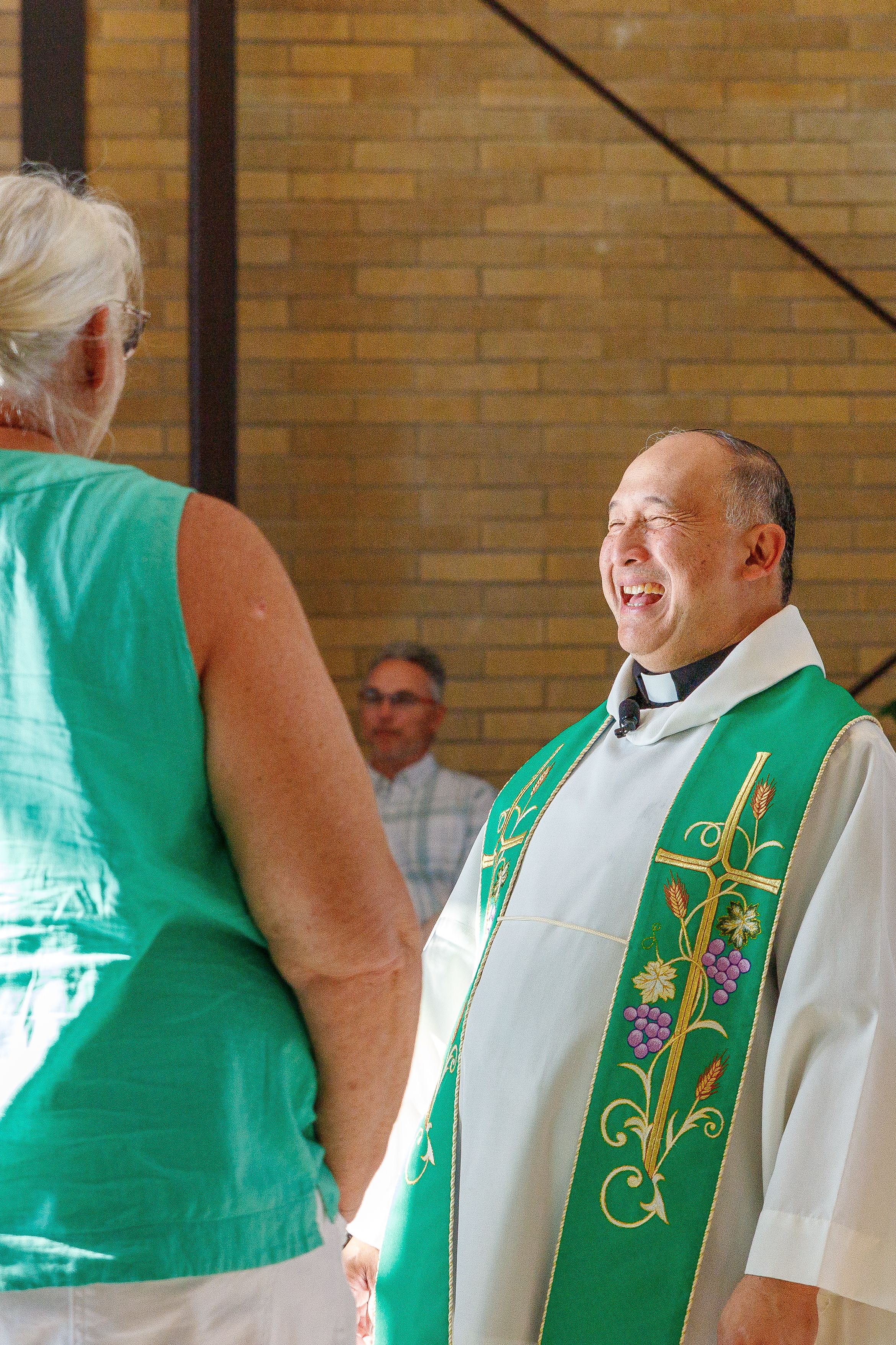 Church leader wearing ceremonial green vestments shares a joyful moment with parishioners.