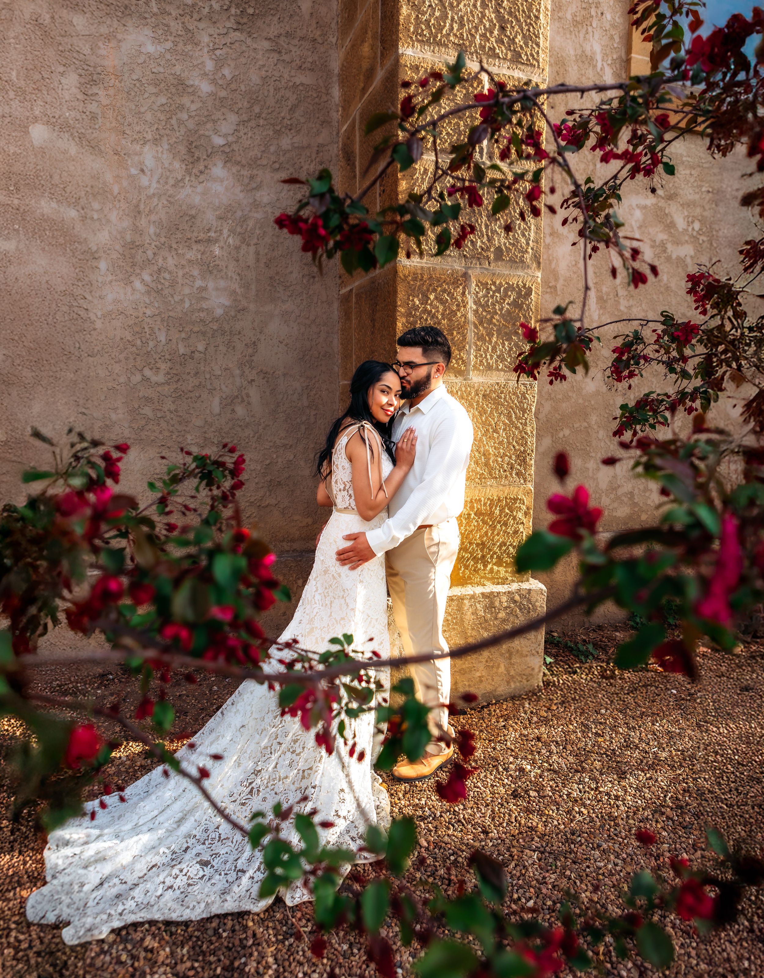 A romantic garden wedding photo session with couple resting on stone wall surrounded by blooming pink bougainvillea flowers.