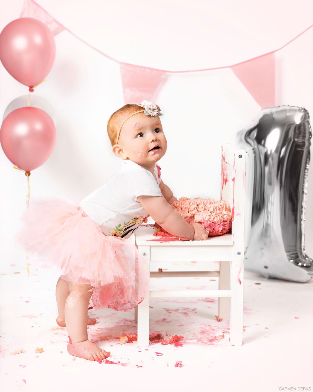 cakesmash photoshoot 1 jaar 
met zacht roze kleuren en ballonnen, kindje staat bij kruk met daarop de taart. in studio in maas en waal
