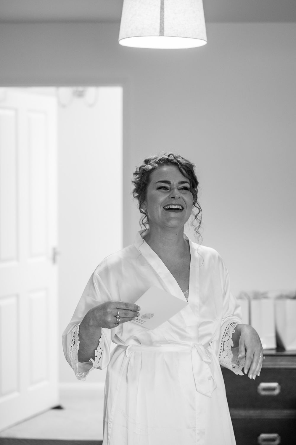 Person in white robe laughing joyfully during wedding morning preparations.