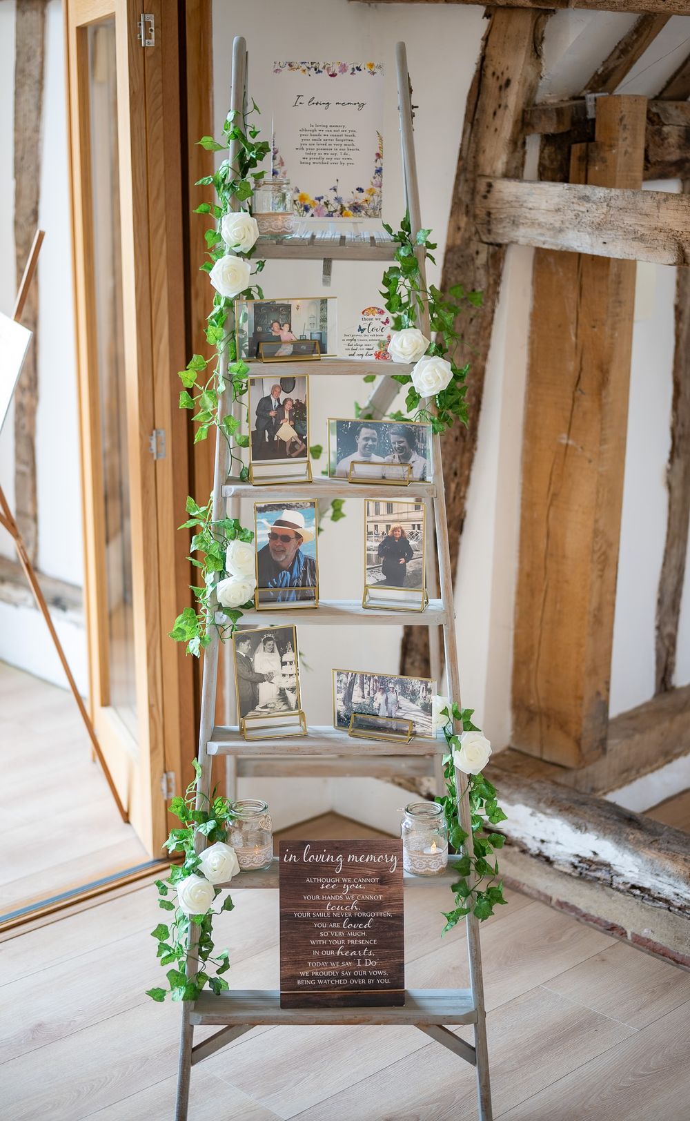 Rustic wedding memory display with vintage photos and greenery decorations on wooden beams.