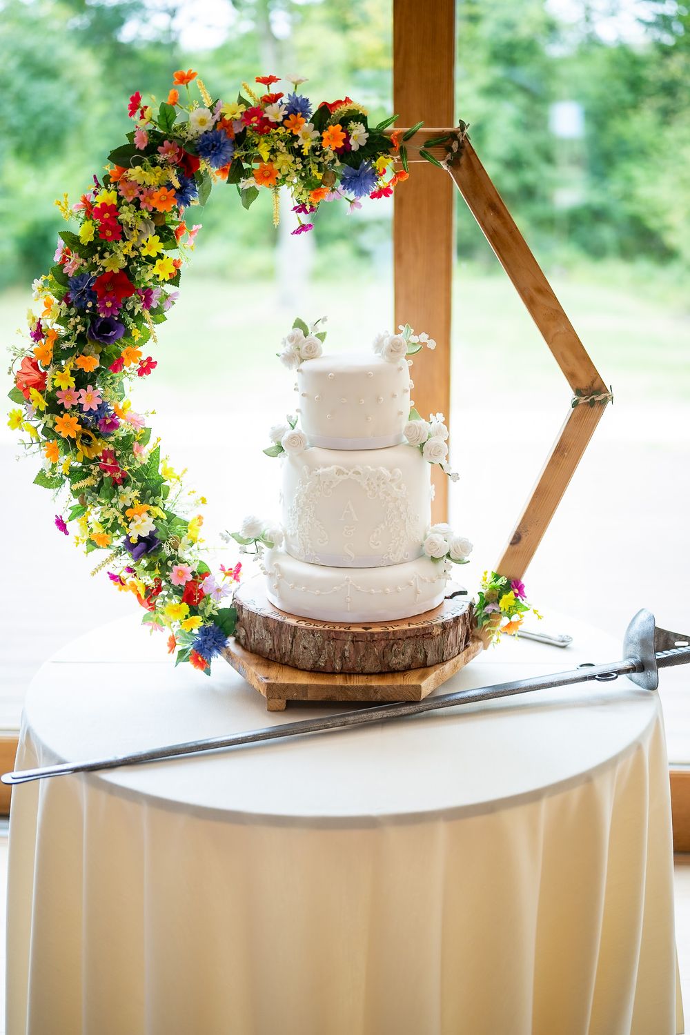 White wedding cake decorated with vibrant wildflowers on a wooden display stand.