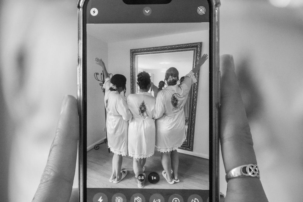 Black and white photo of bridesmaids in matching dresses reflected in mirror.