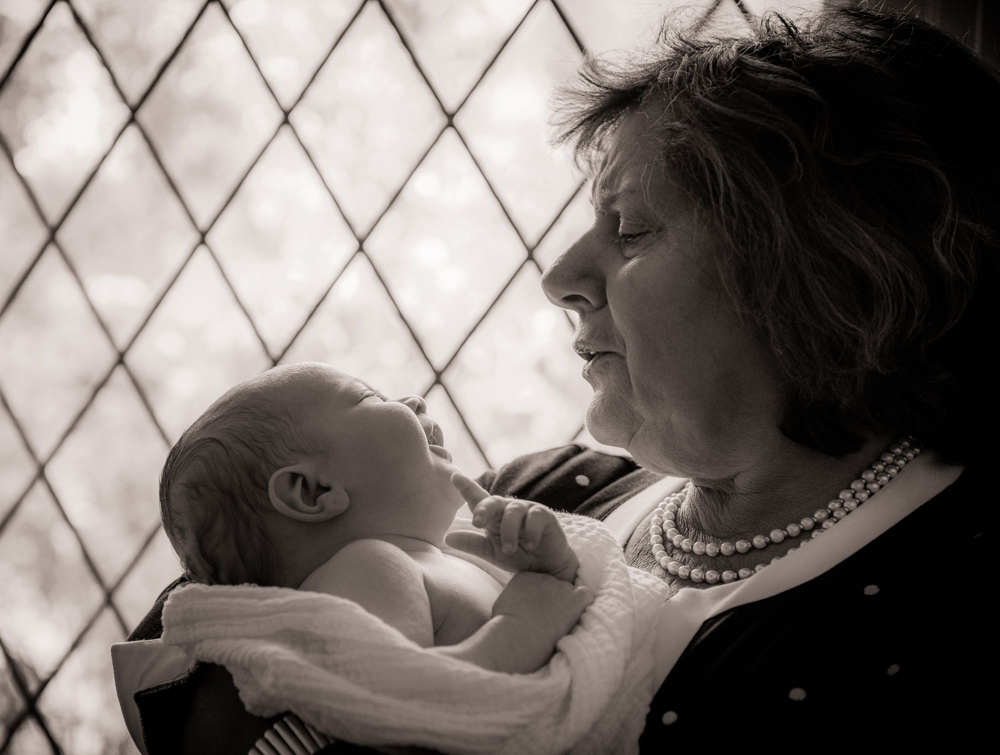 grandma is holding her grandson during the baptism event preparations at home during the photoshoot