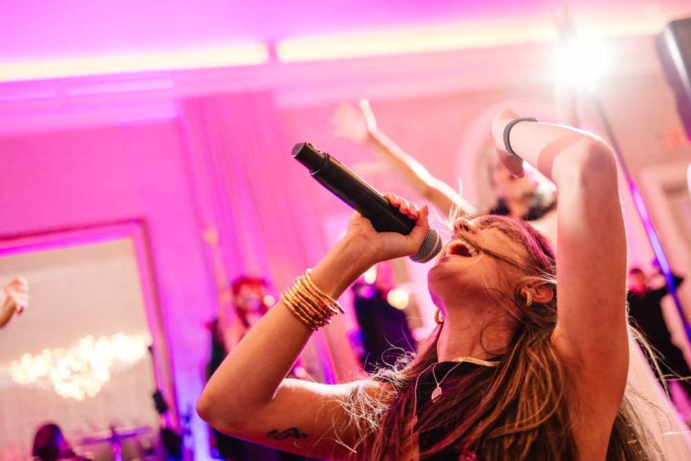 People singing and dancing at a party with vibrant pink lighting and entertainment atmosphere.