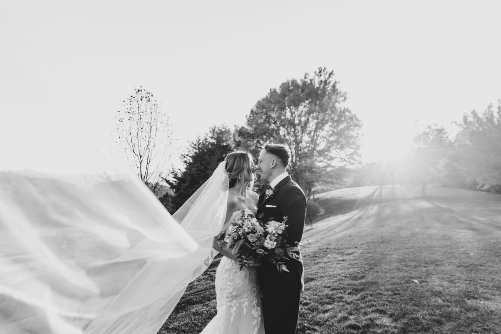 Wedding veil flows dramatically in black and white mountain portrait.