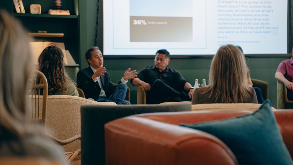 People sit on a panel during an educational presentation with a projection screen visible in the background.