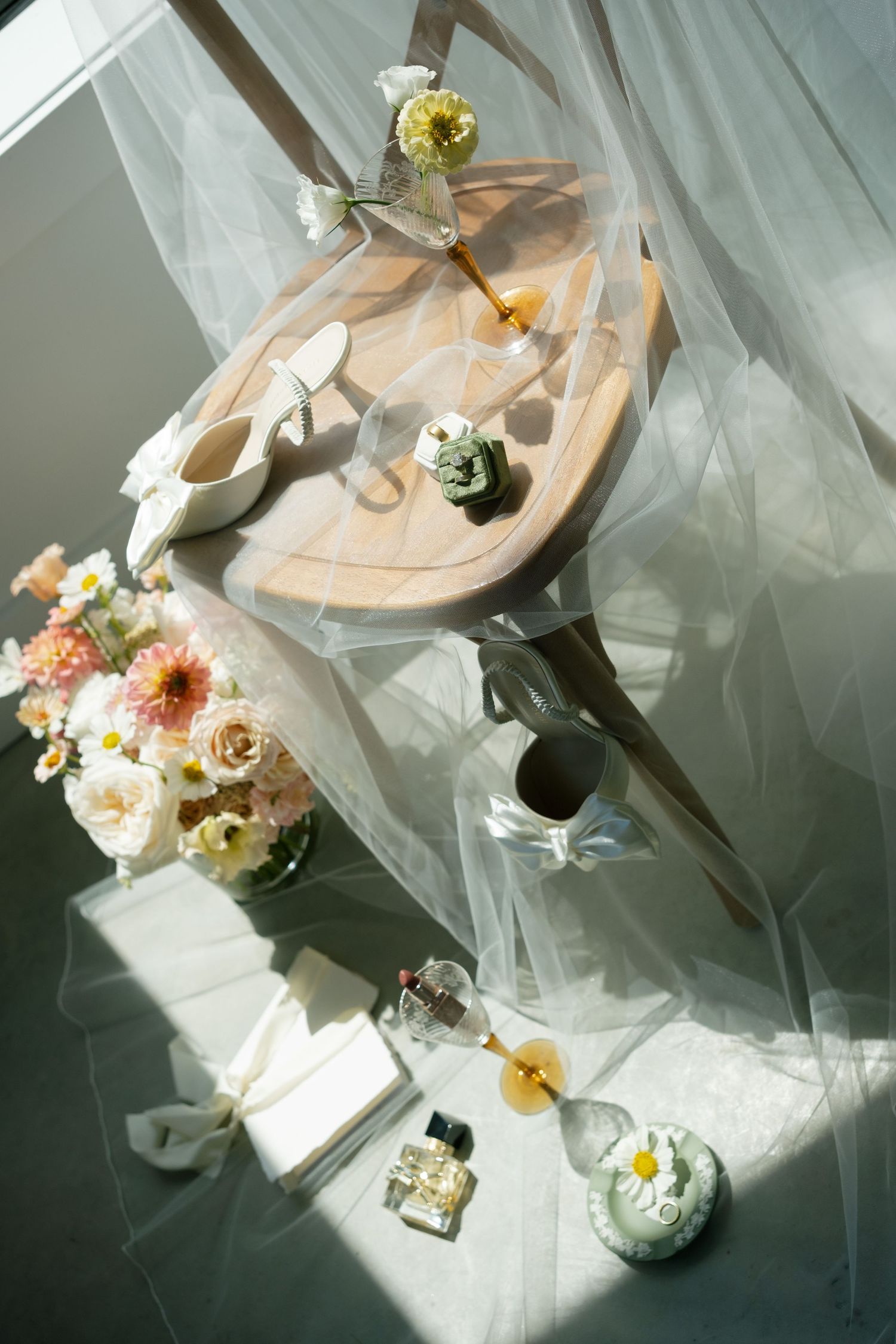 White bridal shoes arranged with green leaves and wedding rings on a light background.