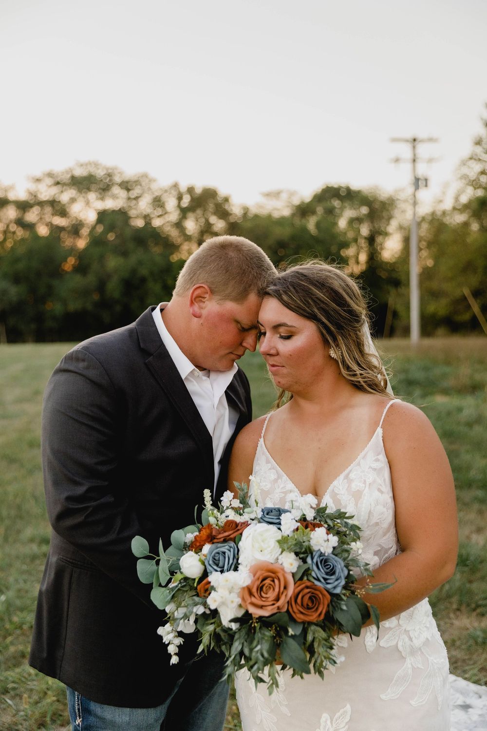Wedding couple embracing outdoors at sunset with beautiful floral bouquet.