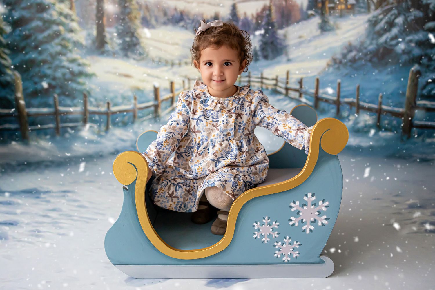 Fotografía infantil de niña en trineo azul con copos de nieve en decorado invernal en el estudio de Rosi López Fotografía en Cuenca