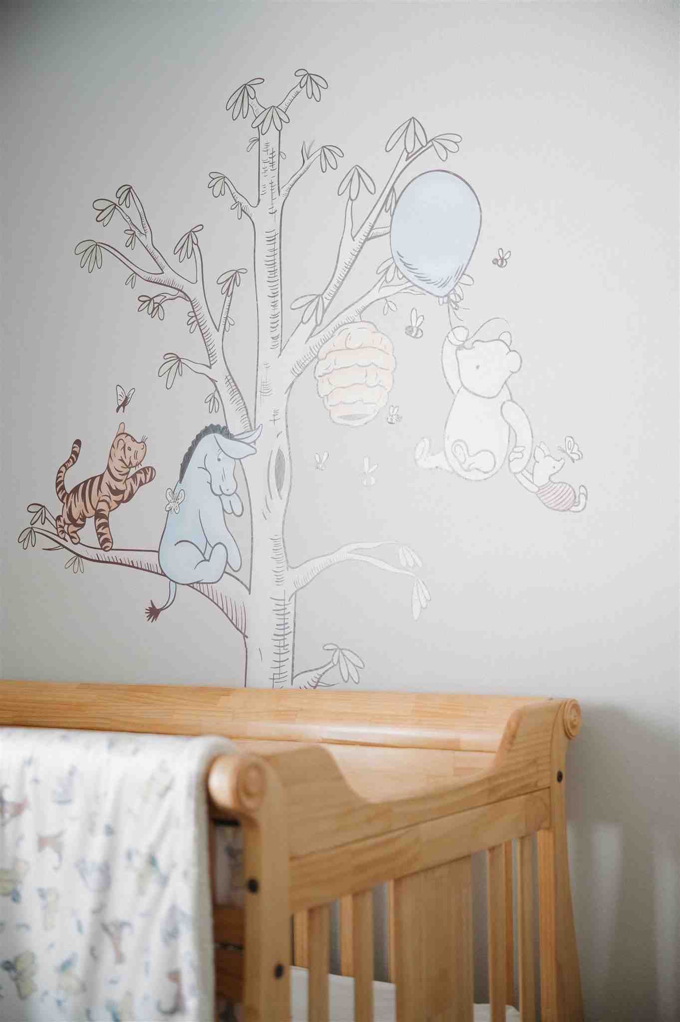 Sweet nursery wall mural featuring whimsical tree branches, animals and a floating balloon above a wooden crib.